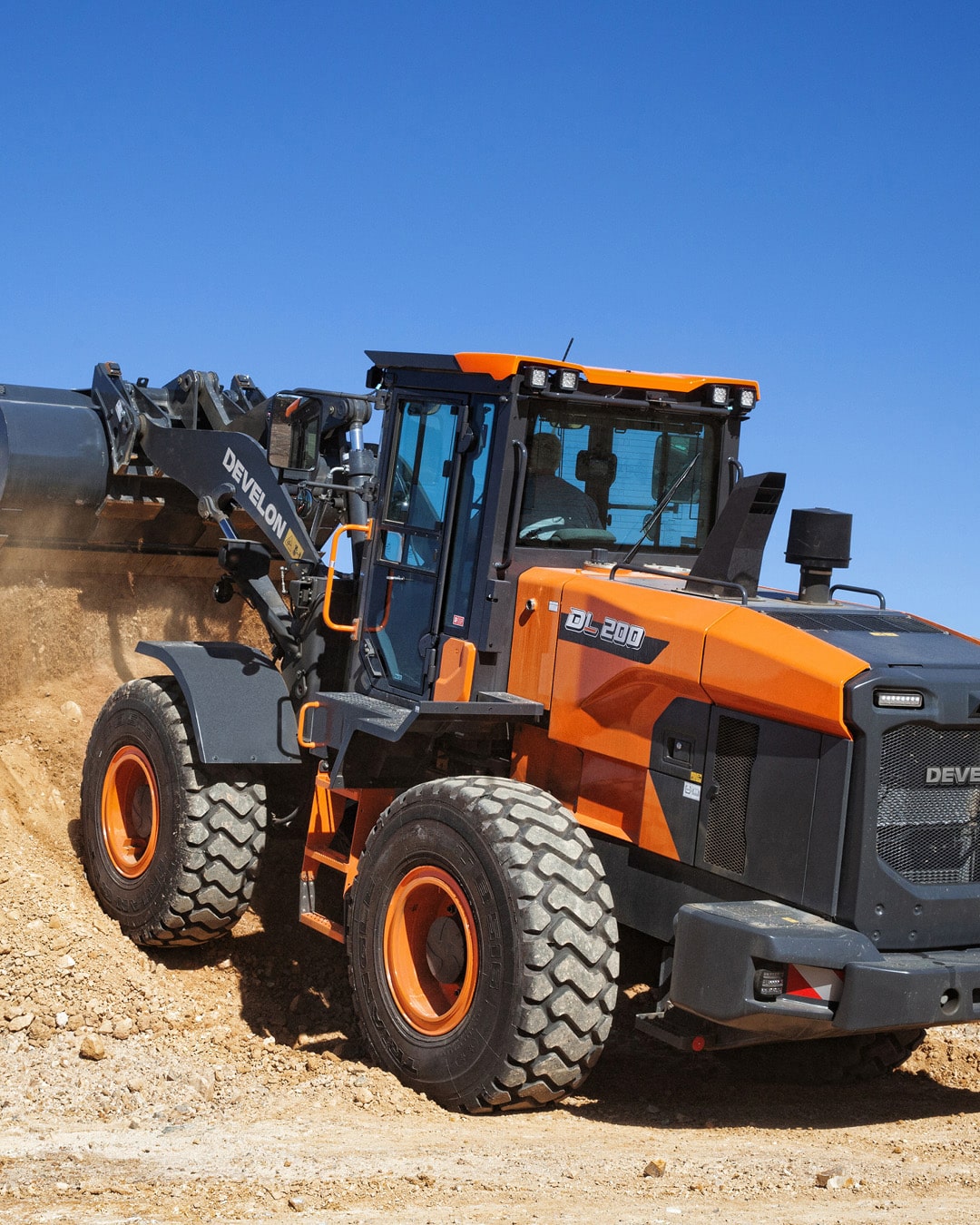 A Develon Wheel Loader manoeuvring on a rugged construction site, efficiently lifting a full bucket of earth, showcasing its power and stability in demanding environments.