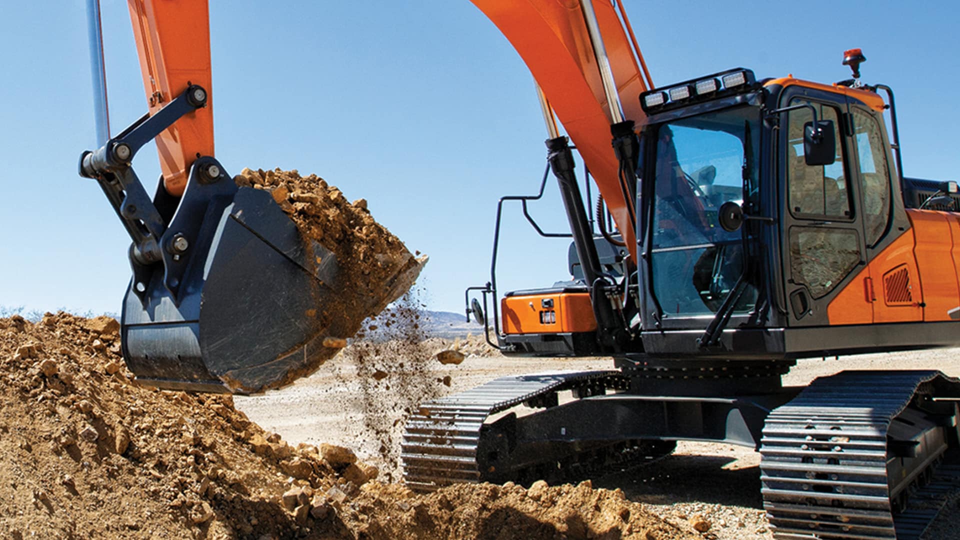 Develon DX225LC-7M Large Excavator lifting and dumping soil on a rugged construction site, showcasing its impressive power and efficiency under a bright blue sky.