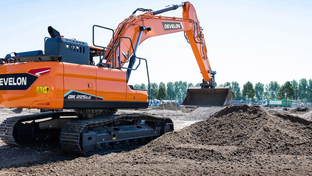Develon DX225LC-7M Large Excavator on a construction site, efficiently moving soil with its robust bucket, highlighting its power and precision under clear skies.