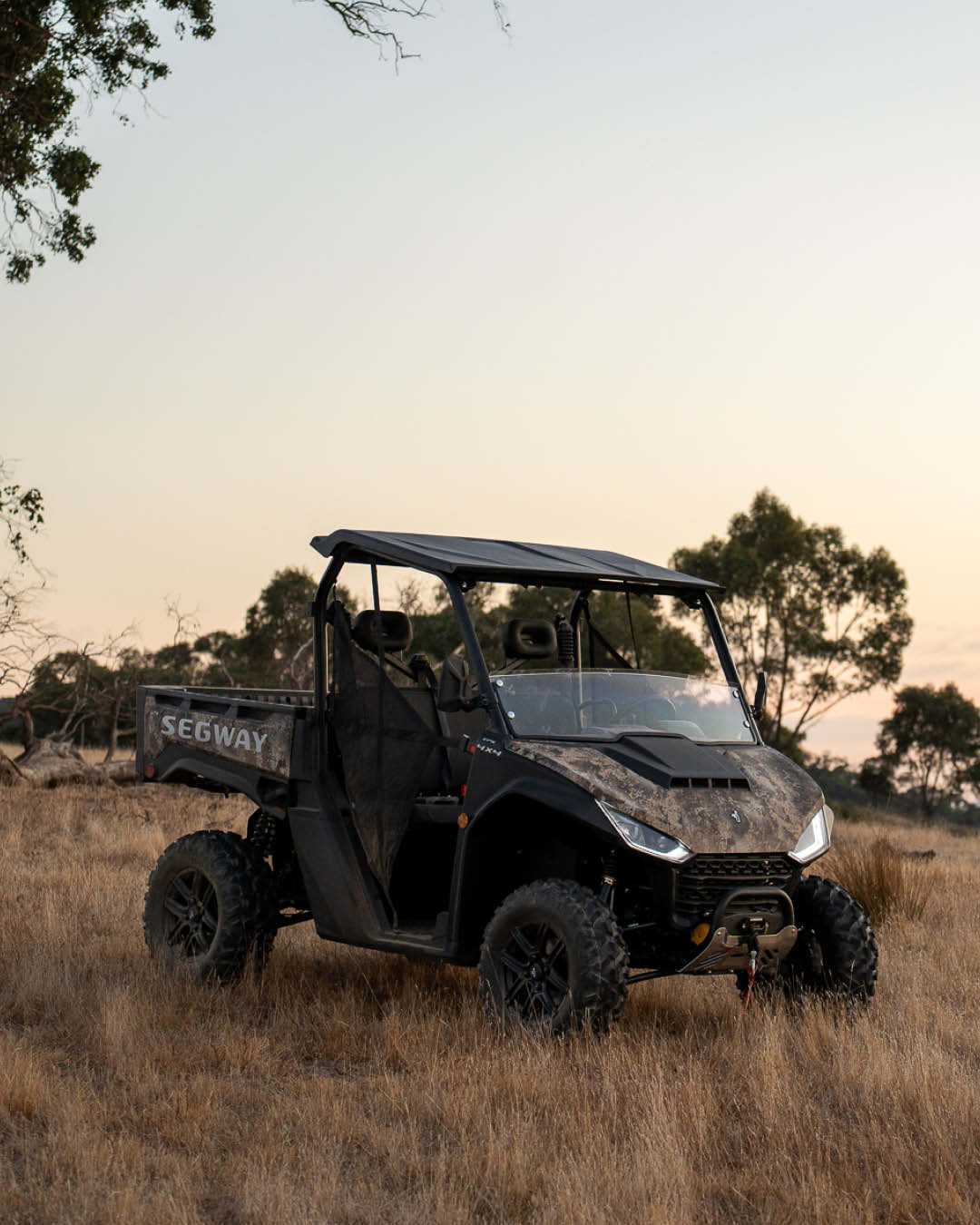 Segway UT6 Navigator UTV parked on dry pasture at dusk, showing off its camo panels, rugged tyres, and side mesh doors — built tough for off-road utility work.