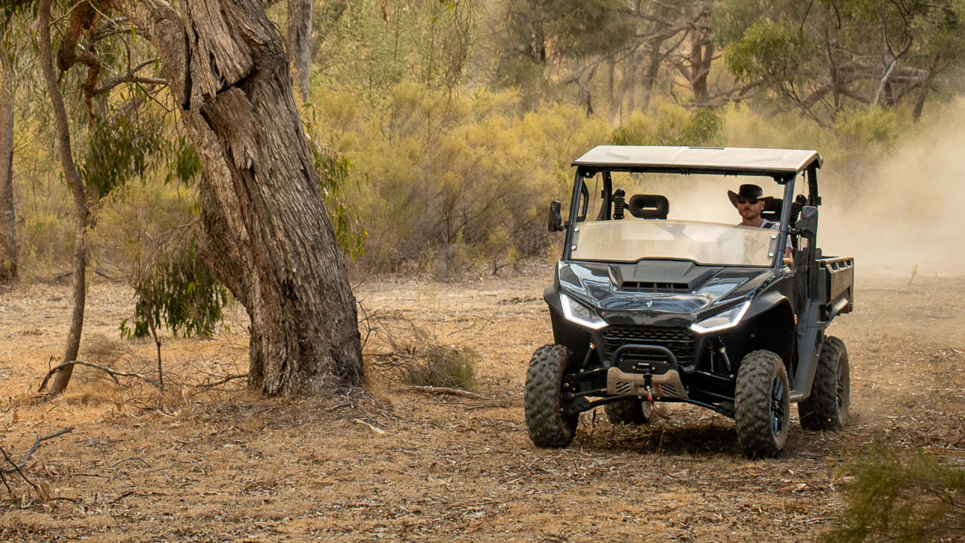 Segway UT6 Navigator UTV kicking up dust on a dry bush trail, driven by a man in a wide-brim hat, showcasing its rugged off-road capability and sleek black design.