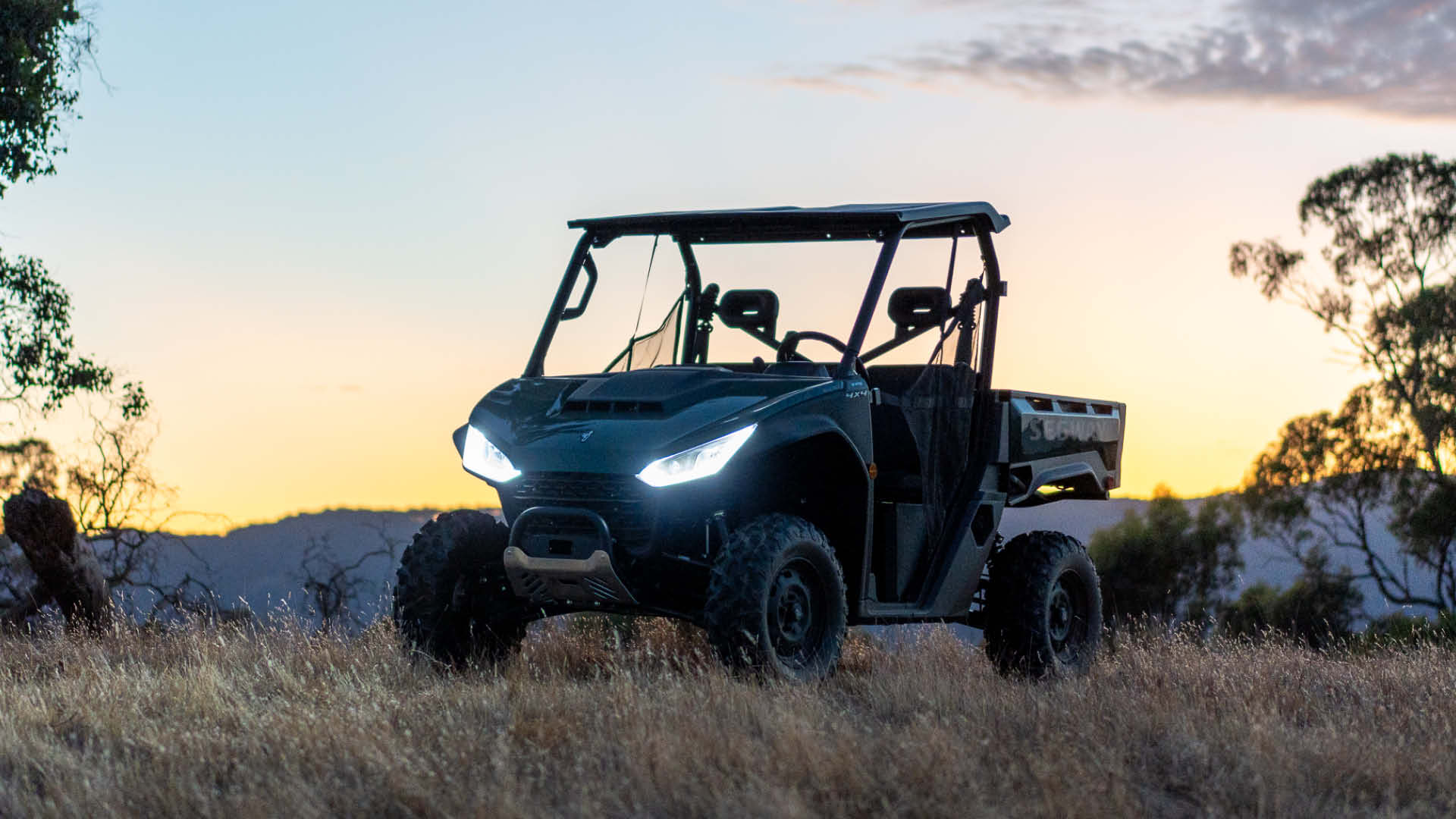 Segway UT6 Rugged EPS UTV with headlights on, parked in dry grass at sunset, showcasing its robust build and off-road readiness in a rural landscape.