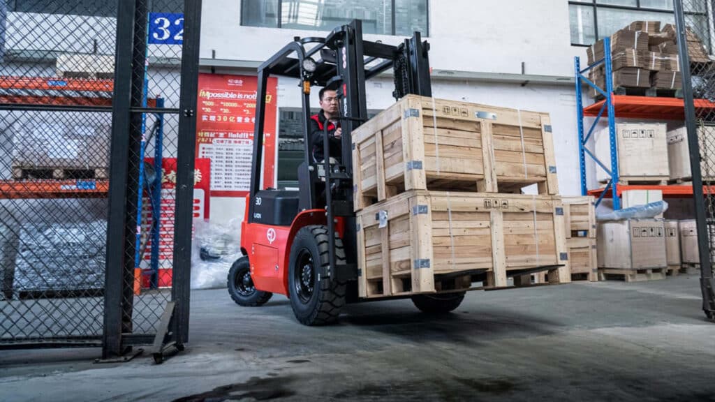 Warehouse worker operating a forklift carrying wooden crates — illustrating the question, how much does it cost to hire a forklift for heavy lifting and logistics tasks.