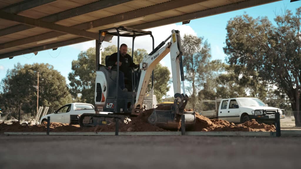 Operator using a Bobcat E17 mini excavator under a shelter, showing one of the top reasons to get a Bobcat E17 — its compact size and versatility on tight job sites.