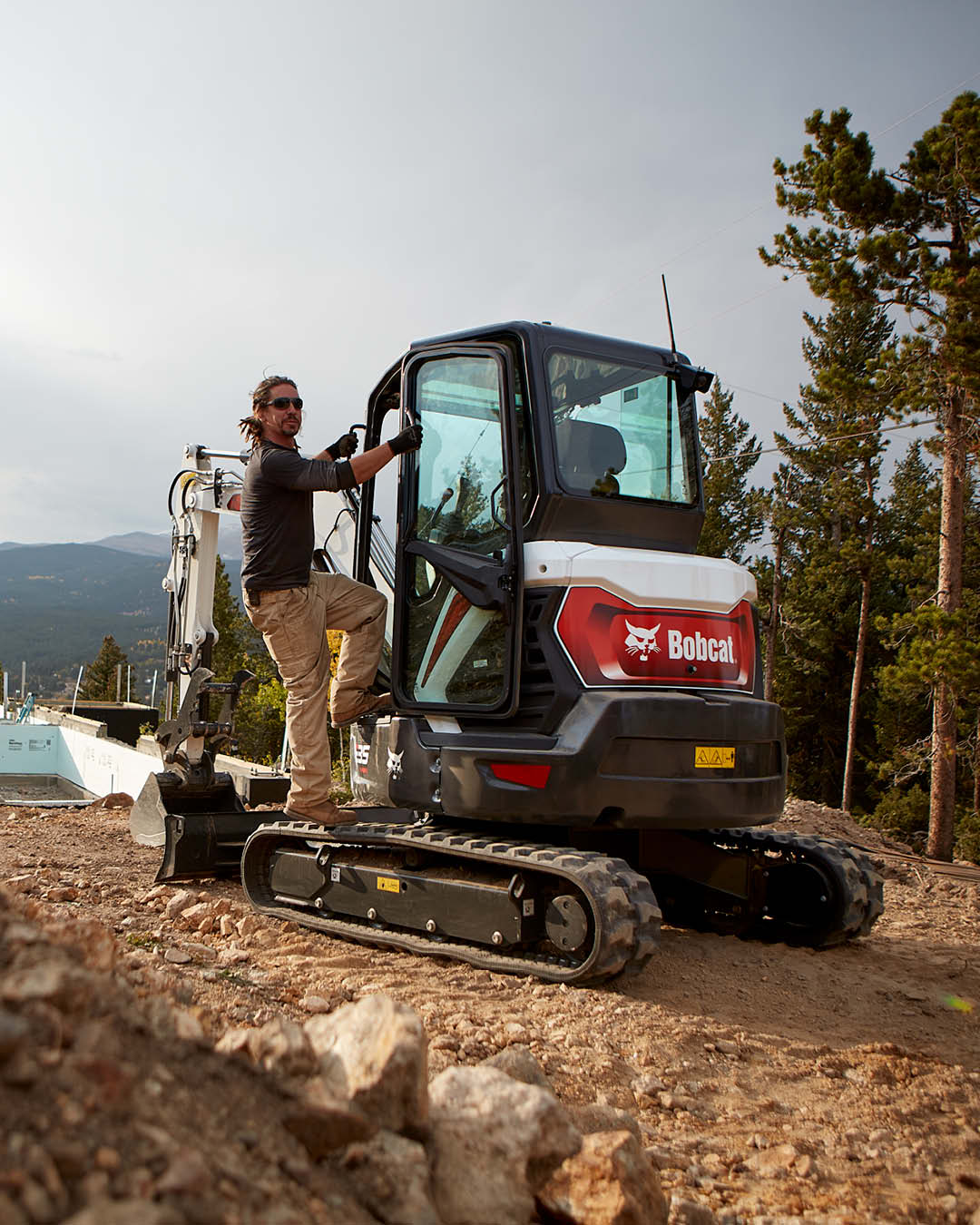 Operator climbing into a Bobcat mini excavator on a rugged job site, backed by Delecca's Service Department to keep machines running strong in tough conditions.