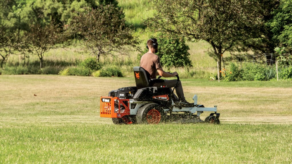 Person operating a Bobcat zero turn mower on a large grassy lawn, demonstrating the maneuverability advantage in the zero turn vs ride on mower comparison.