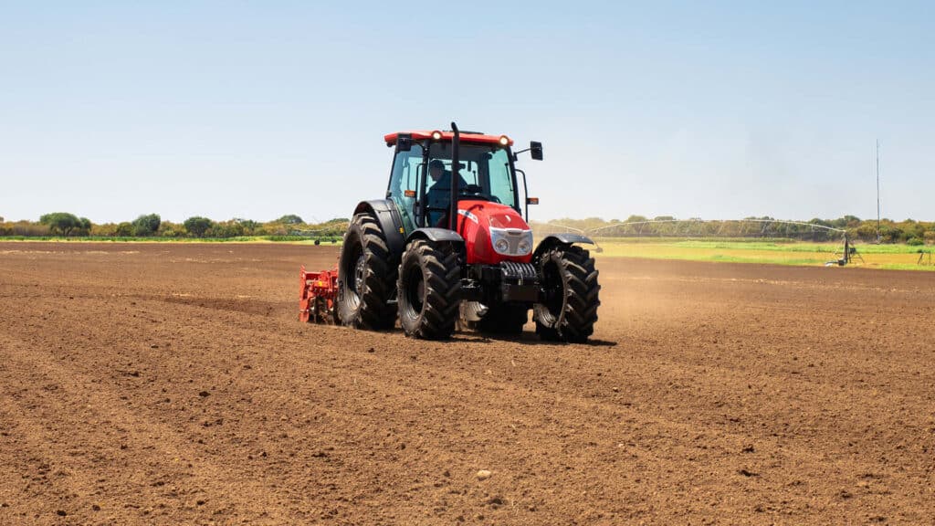 A large red tractor working in a freshly ploughed paddock on a sunny day, illustrating the question: how much does a tractor cost for broadacre farming in Australia?