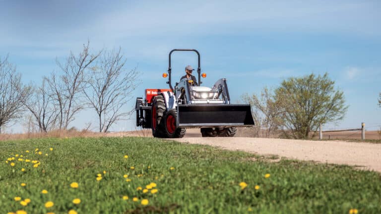 A man operates a Bobcat compact tractor with a front-end loader on a rural property, demonstrating how to choose the right compact tractor for tasks like moving soil and navigating uneven terrain.