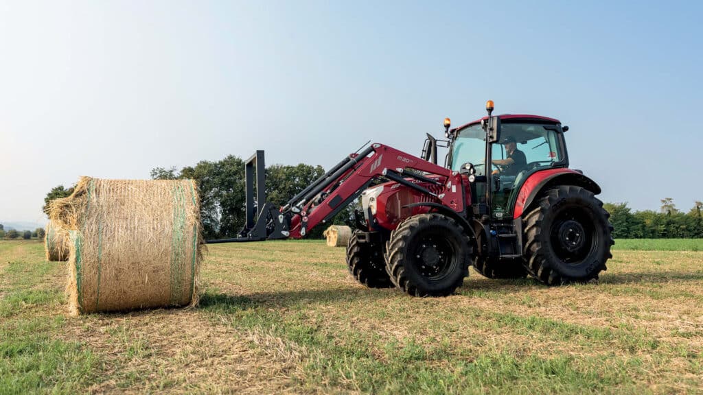 McCormick X5 Series tractor in a hay paddock using a front loader to move round bales — a compact workhorse featured in Delecca’s 0.99% finance campaign.