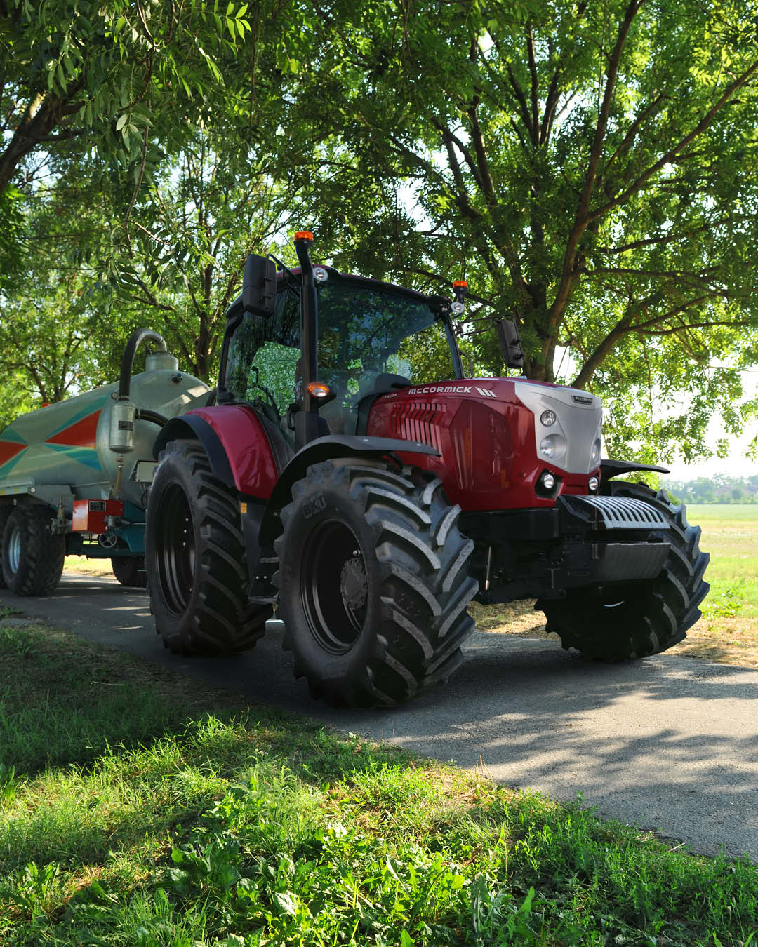 McCormick X6 tractor towing a slurry tank on a rural road under tree shade.