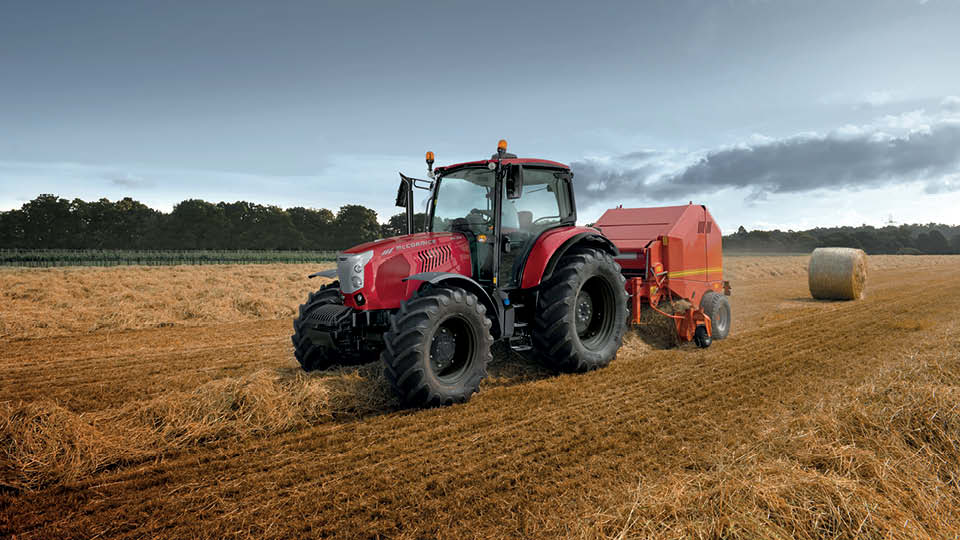 McCormick X6 tractor operating in a hay field, pulling a round baler under cloudy skies – showcasing power and versatility for Australian farms.