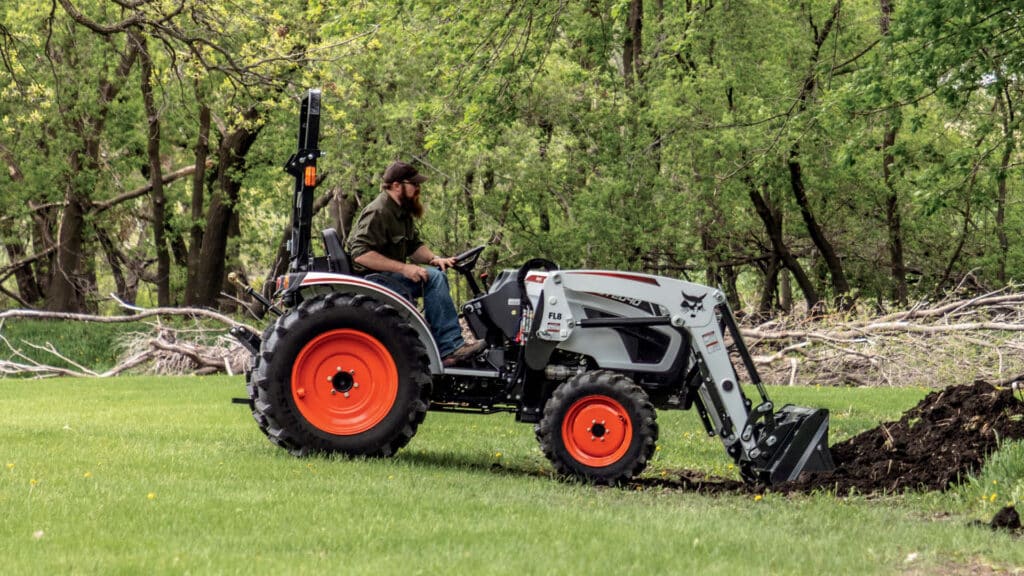 Man operating a Bobcat compact tractor with front-end loader on a rural property, showcasing small tractor for sale in Victoria.