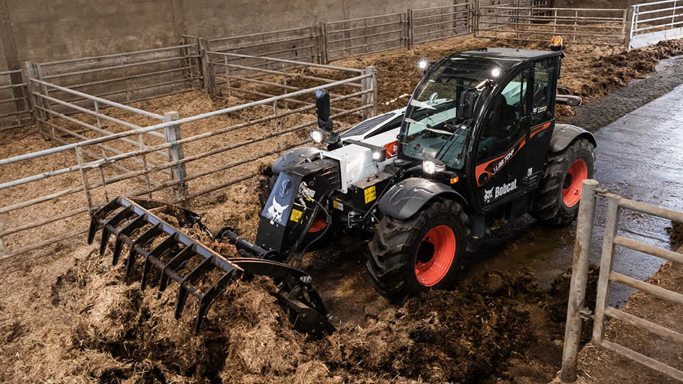Bobcat telehandler cleaning a livestock shed, showing its versatility for handling manure and farm maintenance tasks.