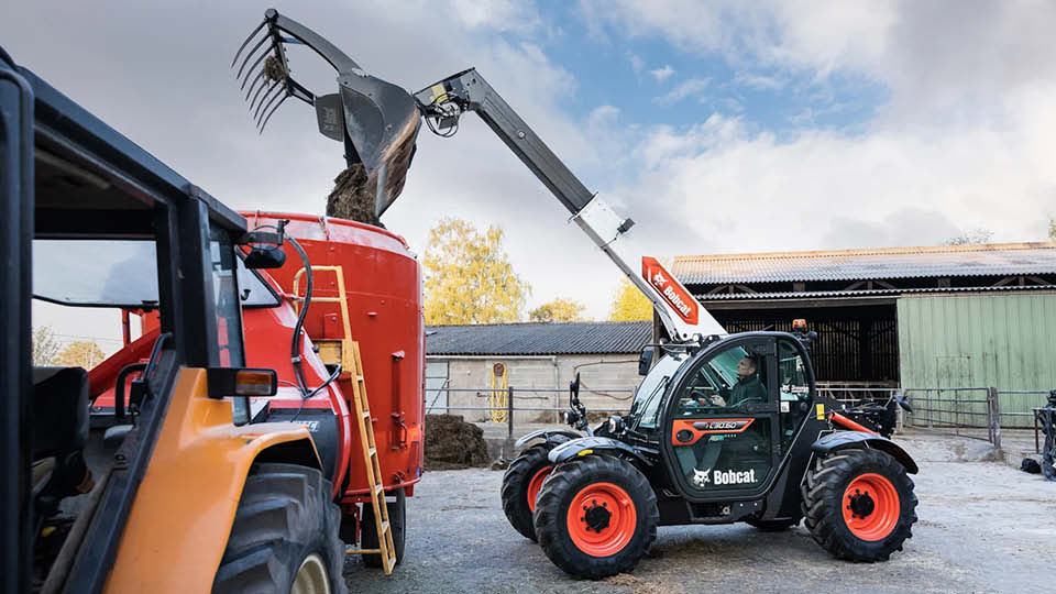 Bobcat telehandler lifting feed into a farm mixer, part of the Bobcat telehandler range for agricultural work.