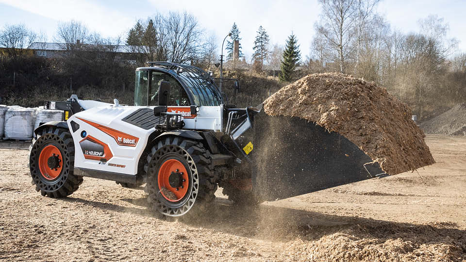 Bobcat telehandler transporting a large load of mulch on a farm, demonstrating powerful lifting and material handling capabilities.