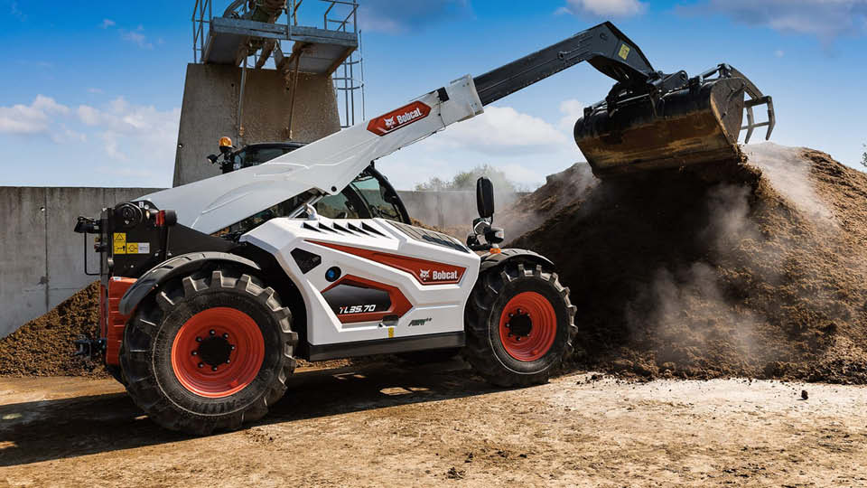 Bobcat telehandler moving a large pile of manure on a farm, demonstrating the machine’s lifting power and versatility.