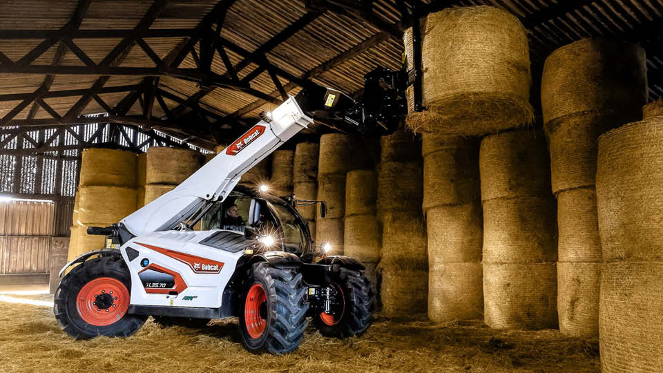 Bobcat TL35.70 telehandler for sale stacking round hay bales in a farm shed, showing high reach and efficiency for agricultural work.