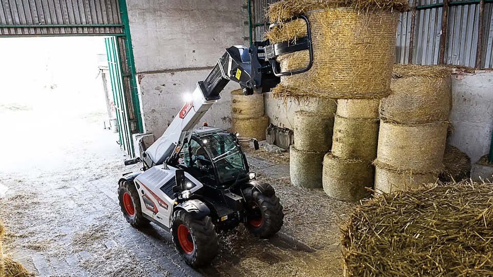 Bobcat TL43.80HF telehandler for sale lifting round hay bales in a farm shed, showing maximum reach and capacity for large agricultural operations.