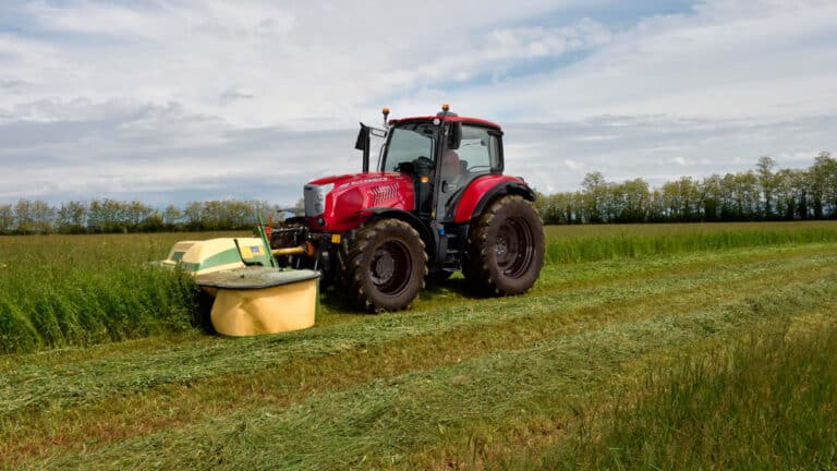 An X6, from the McCormick X Series tractor range, working in a green paddock, cutting pasture with a mower attachment on a farm.