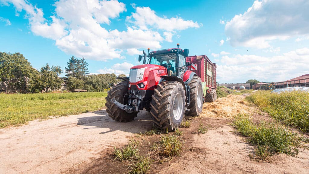 McCormick X8 tractor hauling a large farm trailer loaded with feed on a rural property.
