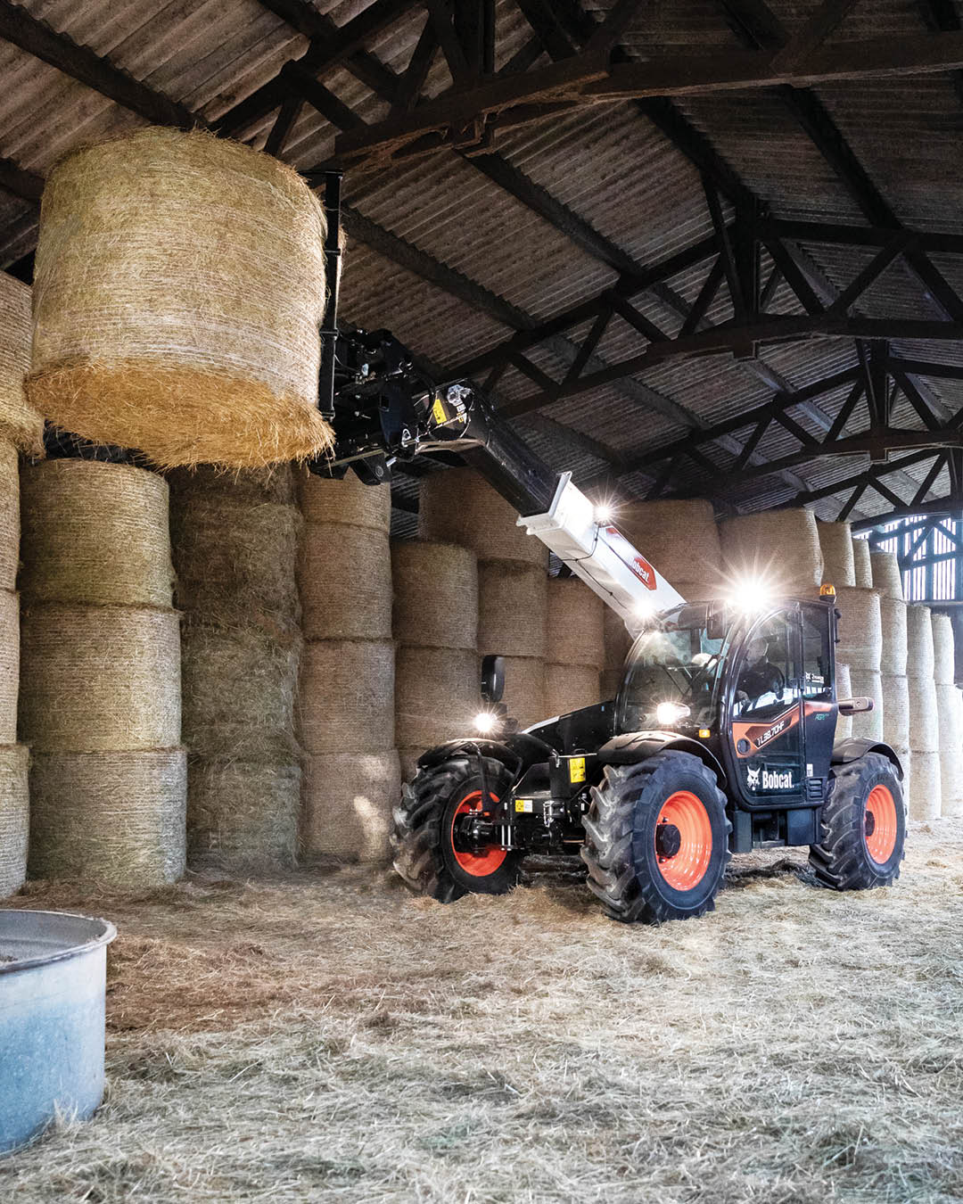 Bobcat TL38.70HF Agricultural Telehandler lifting a large round hay bale inside a barn, showcasing its high reach and handling capability for intensive farming operations.