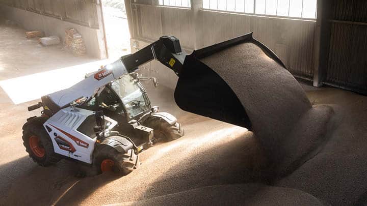 Bobcat agricultural telehandler moving grain in a farm shed, demonstrating daily material handling for farming operations