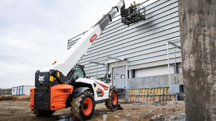 Bobcat construction telehandler on building site with boom extended, positioned near grain silo installation, showing lifting capability for construction and industrial projects