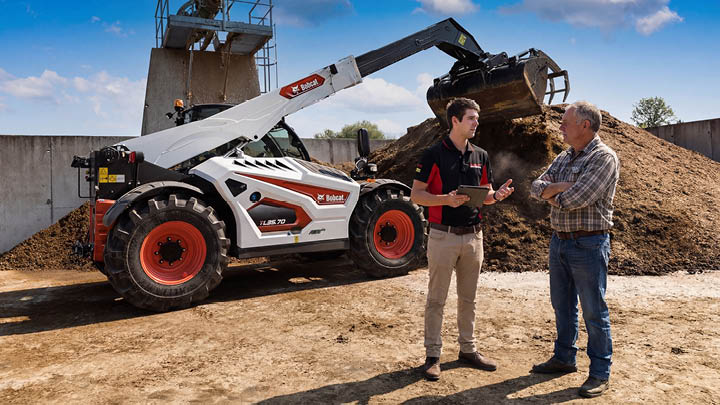 Delecca's team member consulting with farmer about Bobcat agricultural telehandler purchase decision on farm worksite