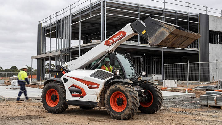 Bobcat TL30.60 construction telehandler operating on a commercial building site in central Victoria, operator in cab, hi-vis worker in background
