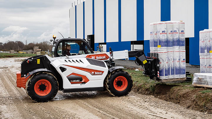 Bobcat TL30.60 compact construction telehandler handling insulation materials beside a commercial building on an unprepared site