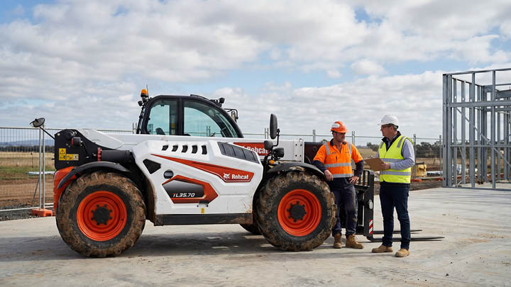 Bobcat TL35.70 construction telehandler stationary on a commercial construction site in central Victoria, construction worker and site manager in discussion beside the machine