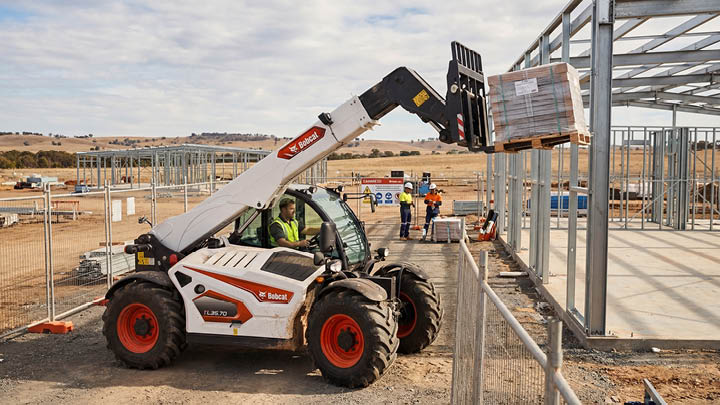 Bobcat TL35.70 construction telehandler placing a pallet of materials into a steel frame structure on a regional construction site in Victoria, workers visible in background
