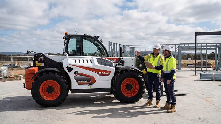 Bobcat TL35.70 construction telehandler stationary on a commercial construction site in Victoria, operator and site manager in consultation beside the machine