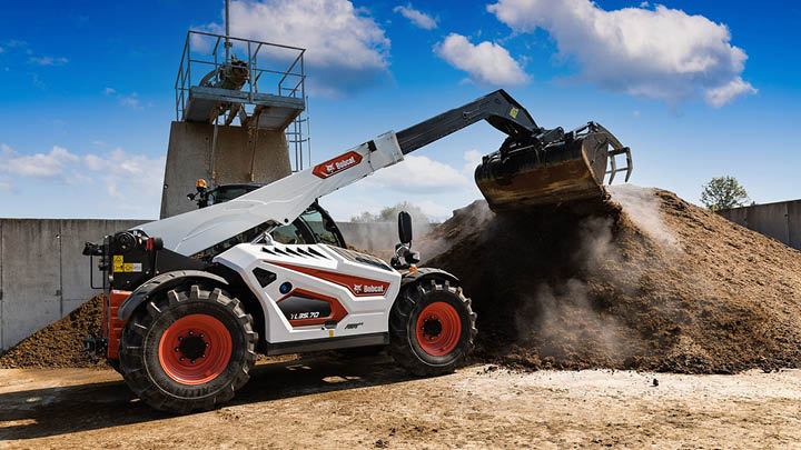 Bobcat TL35.70 agricultural telehandler dumping bulk material with bucket attachment on farm worksite