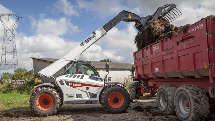 Bobcat TL35.70 agricultural telehandler loading silage into trailer with grapple fork attachment on farm