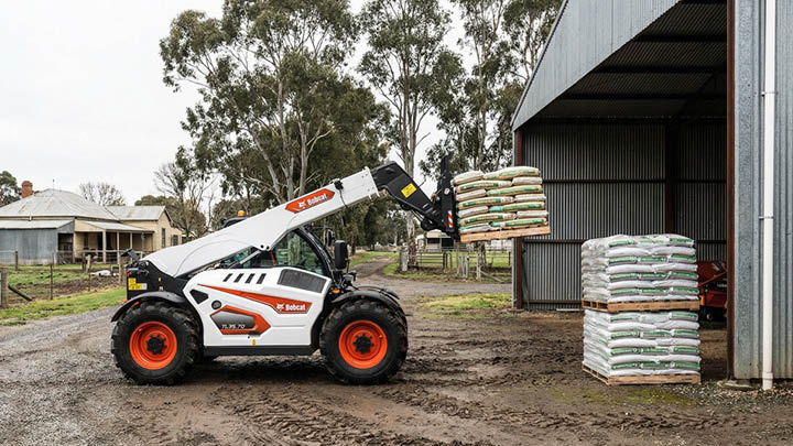 Bobcat TL35.70 agricultural telehandler with pallet forks stacking fertiliser bags on pallets at farm shed, regional Victoria