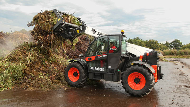 Bobcat TL38.70HF agricultural telehandler moving bulk compost in farm yard with grab bucket attachment