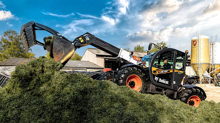 Bobcat TL38.70HF agricultural telehandler handling green silage at feed pit with grain silo in background