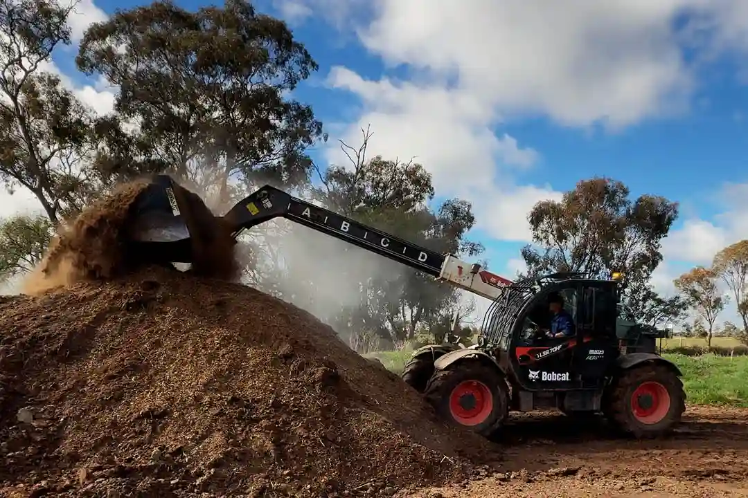 Bobcat agricultural telehandler moving composted manure on Australian farm with eucalyptus trees in background