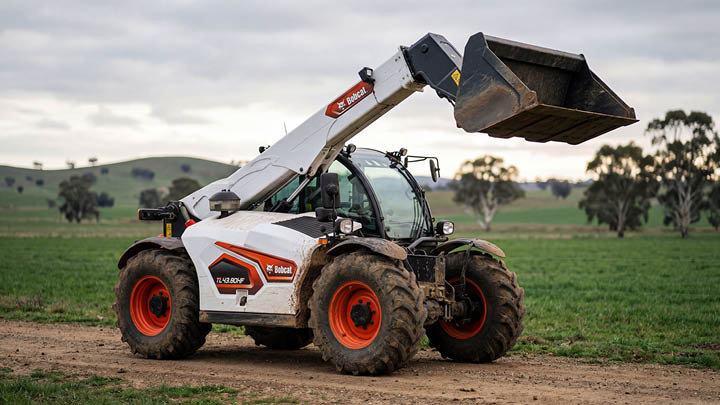 Bobcat TL43.80HF agricultural telehandler on a Central Victorian farm, boom raised with bucket attachment, showing realistic working wear on open pasture