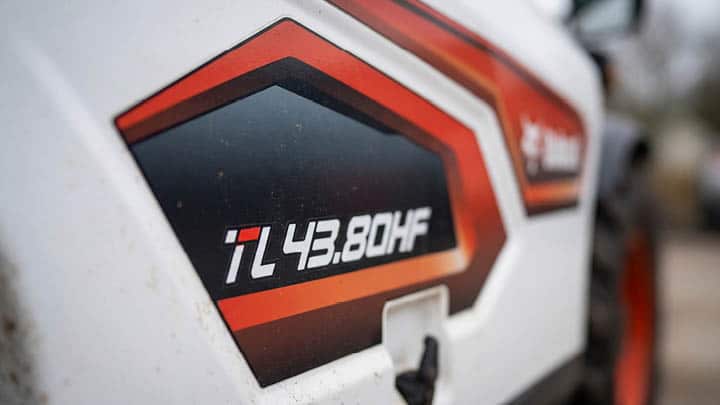 Close-up detail of Bobcat TL43.80HF model decal on agricultural telehandler body panel, showing angular dark panel with white and red lettering